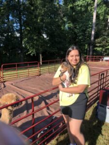A student holds a Bassett hound puppy next to an enclosure at an animal encounter event on campus.